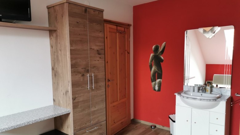 Zimmer mit roter Wand, Holzschrank, Waschbecken und Spiegel.