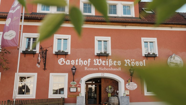 Fassade des Gasthofs Weißes Rössl in Mühldorf mit roter Wand und weißen Fenstern.