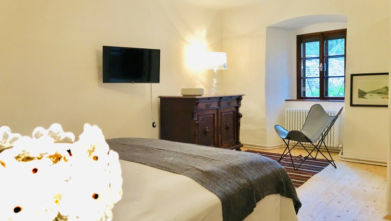 Gemütliches Schlafzimmer mit Bett, antiker Kommode, Sessel und Wand-TV.