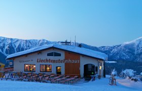 Winterlandschaft mit Liechtensteinhaus und Seilbahn vor schneebedeckten Bergen.