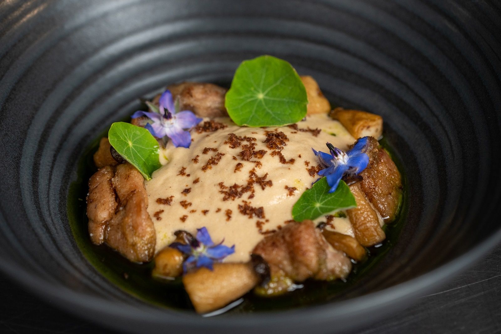 Ein elegantes Gericht in einer schwarzen Schale, dekoriert mit essbaren Blüten und grünen Blättern.