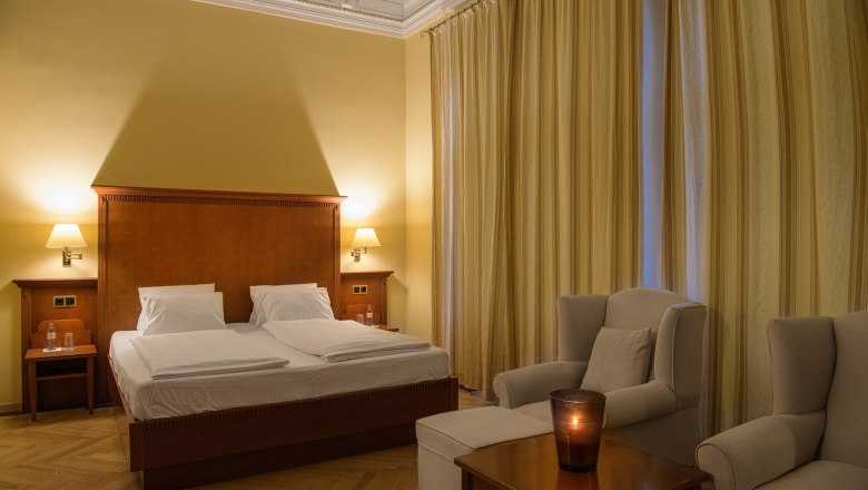 Elegantes Doppelzimmer mit großem Bett, zwei Sesseln und einem Tisch mit Kerze.