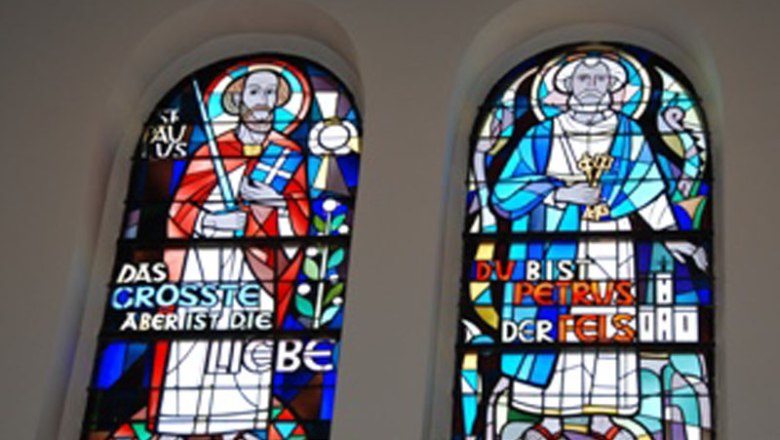 Zwei bunte Kirchenfenster mit religiösen Figuren und Inschriften.