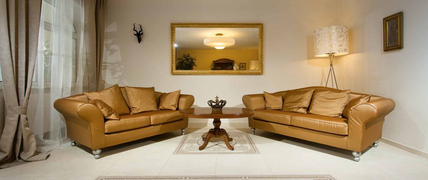 Elegante Lobby mit zwei braunen Sofas, einem runden Holztisch und einem großen Spiegel an der Wand.