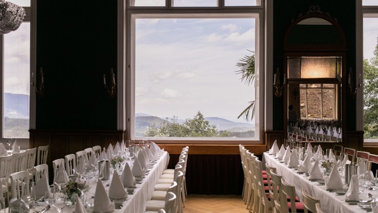 Eleganter Speisesaal mit gedeckten Tischen und Blick auf die Berge durch ein großes Fenster.