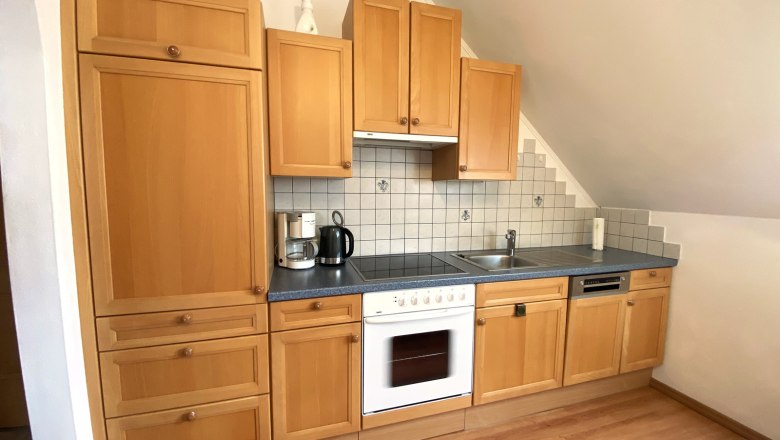 K&uuml;chenzeile mit Holzschr&auml;nken, Herd, Sp&uuml;le und Fliesenr&uuml;ckwand.