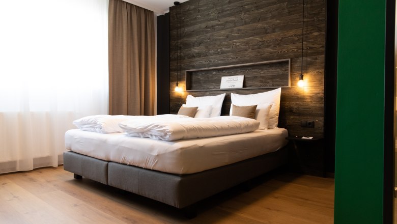 Modernes Hotelzimmer mit gro&szlig;em Bett, Holzwand und h&auml;ngenden Lampen.