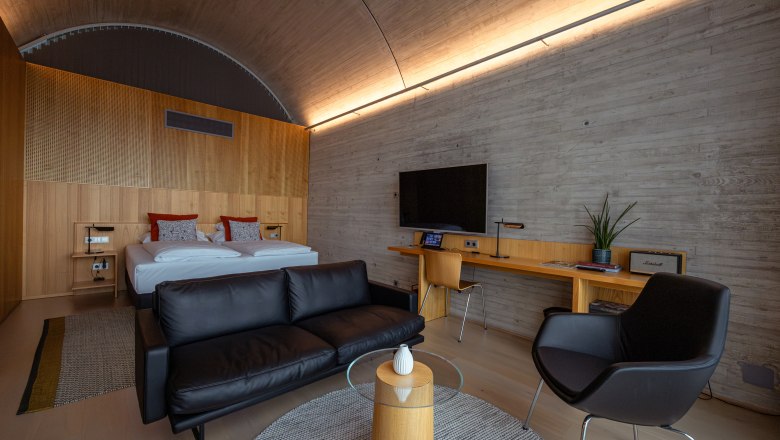 Modernes Hotelzimmer mit Doppelbett, Ledersofa, Schreibtisch und Fernseher.