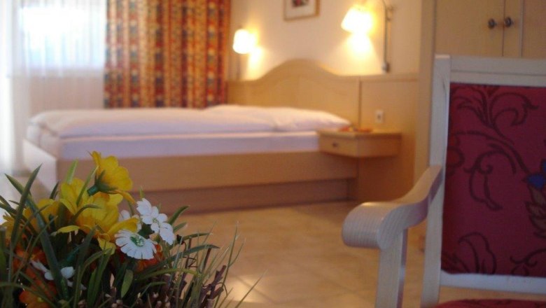 Ein gemütliches Gästezimmer mit einem Bett, einem Stuhl und einem Tisch mit Blumen.