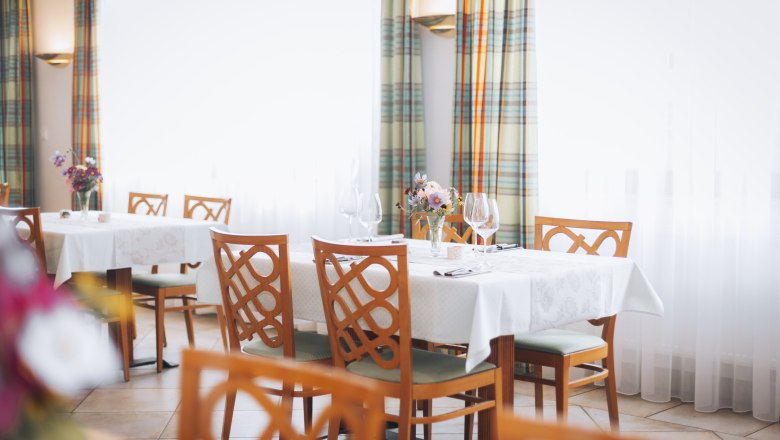 Elegantes Restaurant mit gedeckten Tischen, Blumenarrangements und Weingläsern.