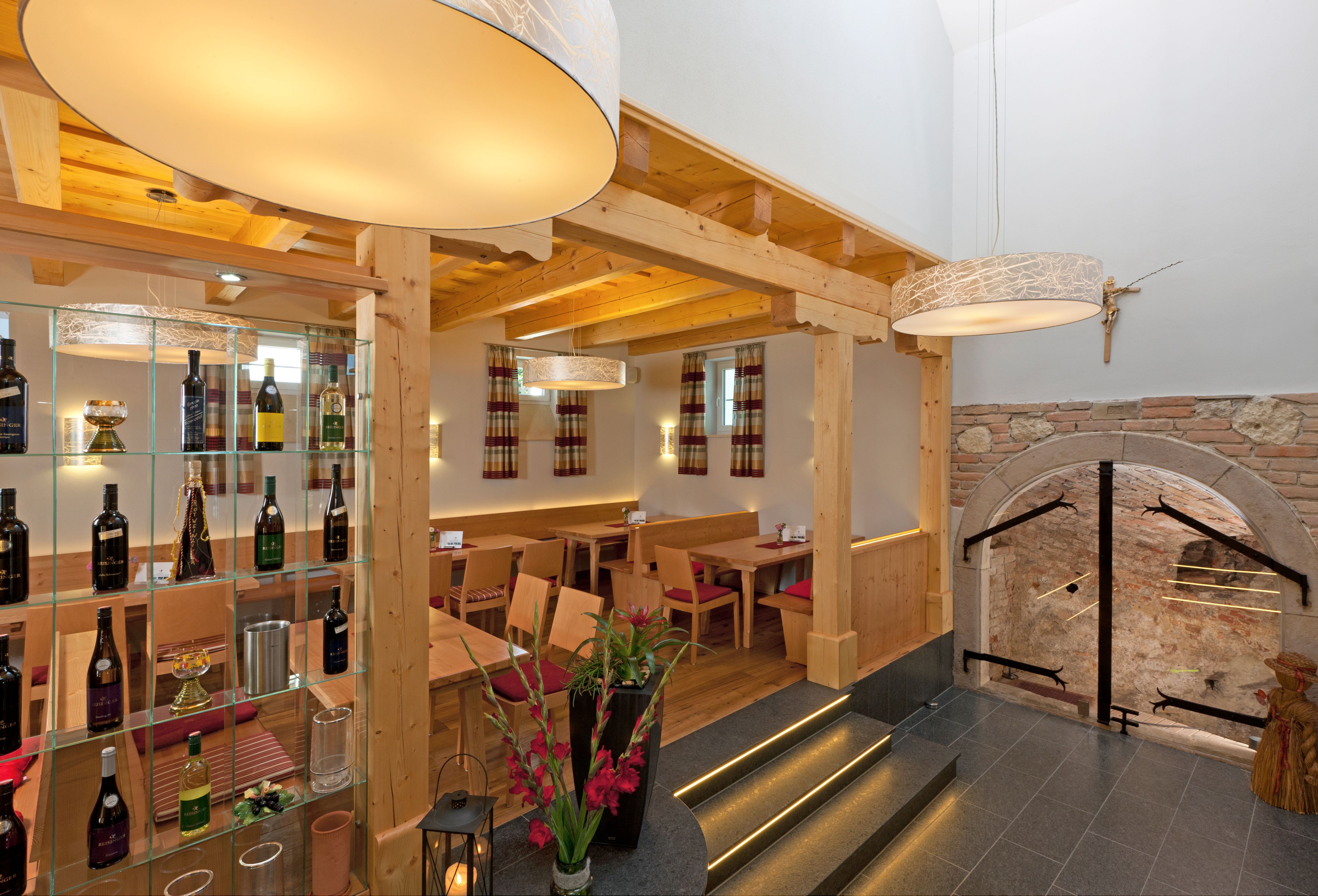 Innenansicht eines Heurigen mit Holzmöbeln, Weinregal und dekorativen Lampen.