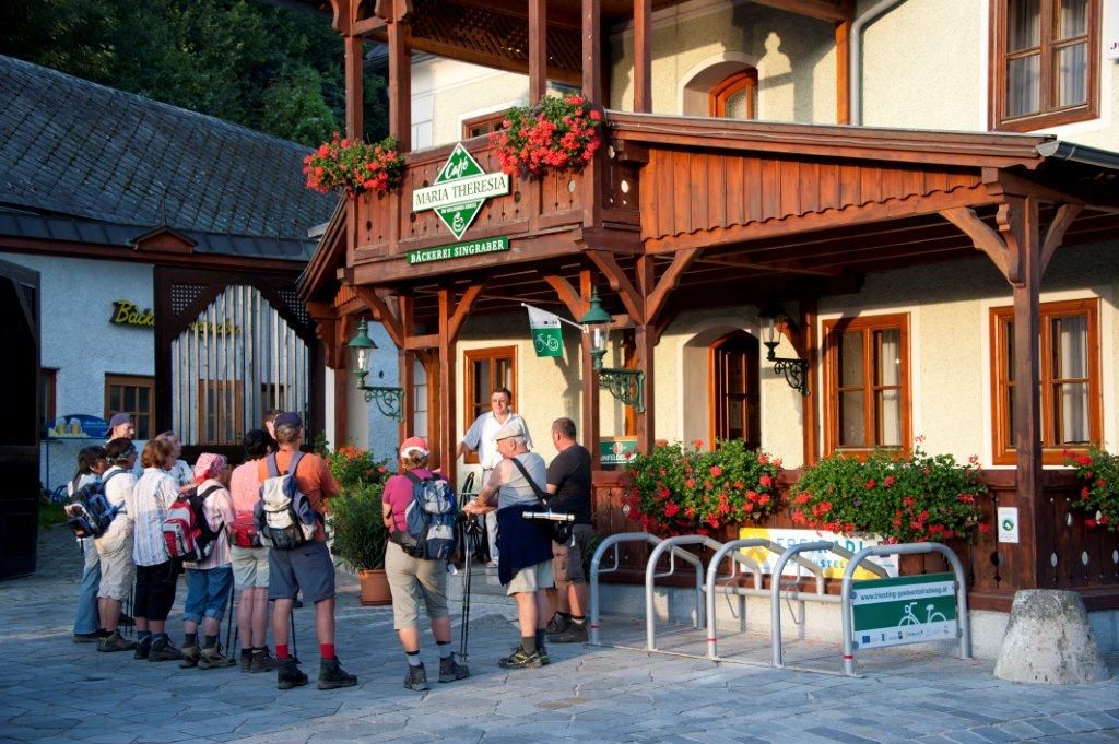 Eine Gruppe von Wanderern steht vor dem Café Maria Theresia mit Holzveranda und Blumendekoration.
