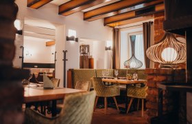 Gemütliches Restaurant mit Holzbalken, grünen Polsterstühlen und dekorativen Lampen.