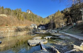 Eingangsbereich der Myrafälle mit Teich, Bänken und umliegenden Bäumen.