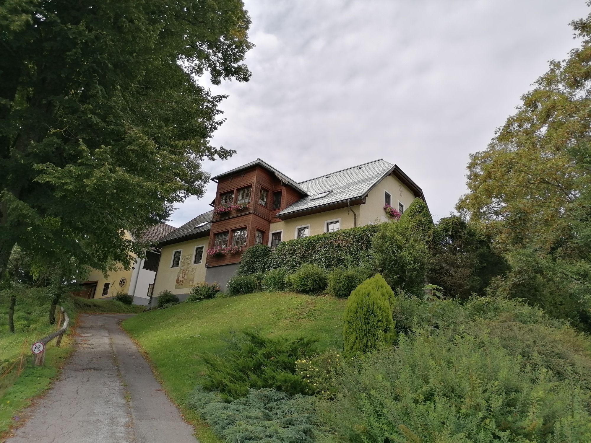 Ein großes Haus auf einem Hügel mit Bäumen und einem Weg im Vordergrund.