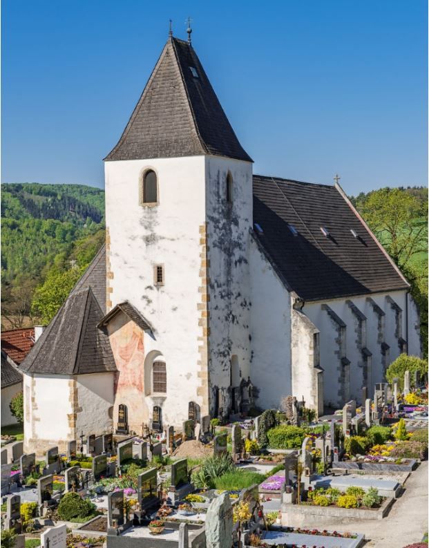 Rustikale Wehrkirche Bromberg mit breitem Turm und Friedhof im Vordergrund.