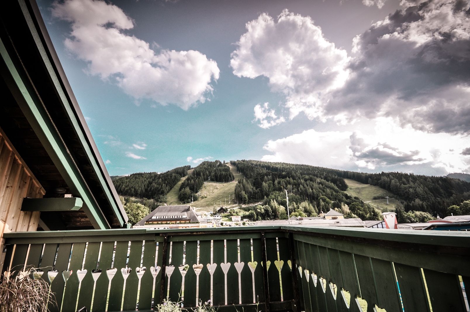 Blick von einem Balkon auf eine grüne Berglandschaft mit Wolken am Himmel.