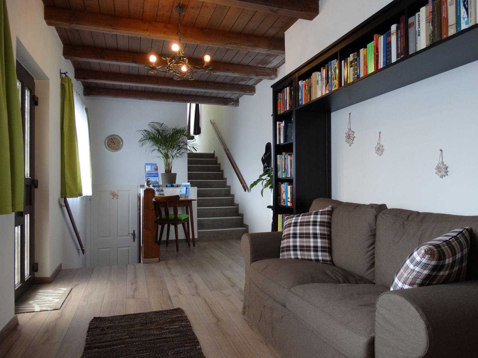 Wohnzimmer mit braunem Sofa, Bücherregal und Treppe im Hintergrund.