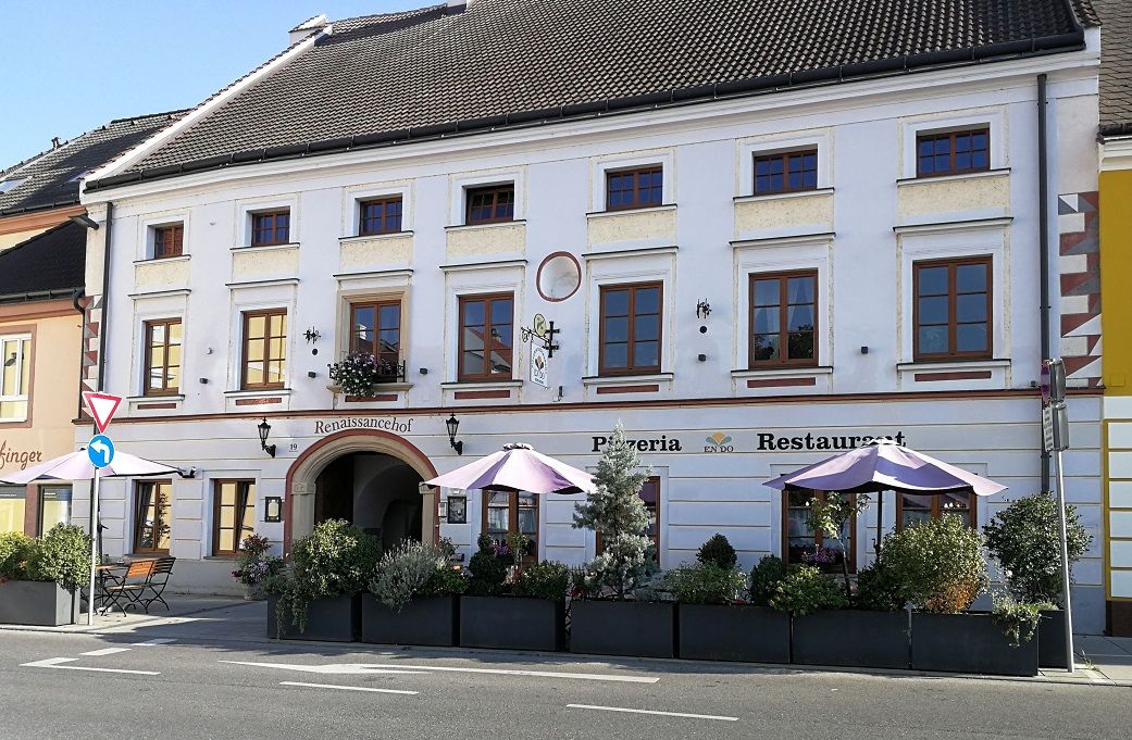 Historisches Gebäude mit Pizzeria und Restaurant, dekoriert mit Pflanzen und Sonnenschirmen.