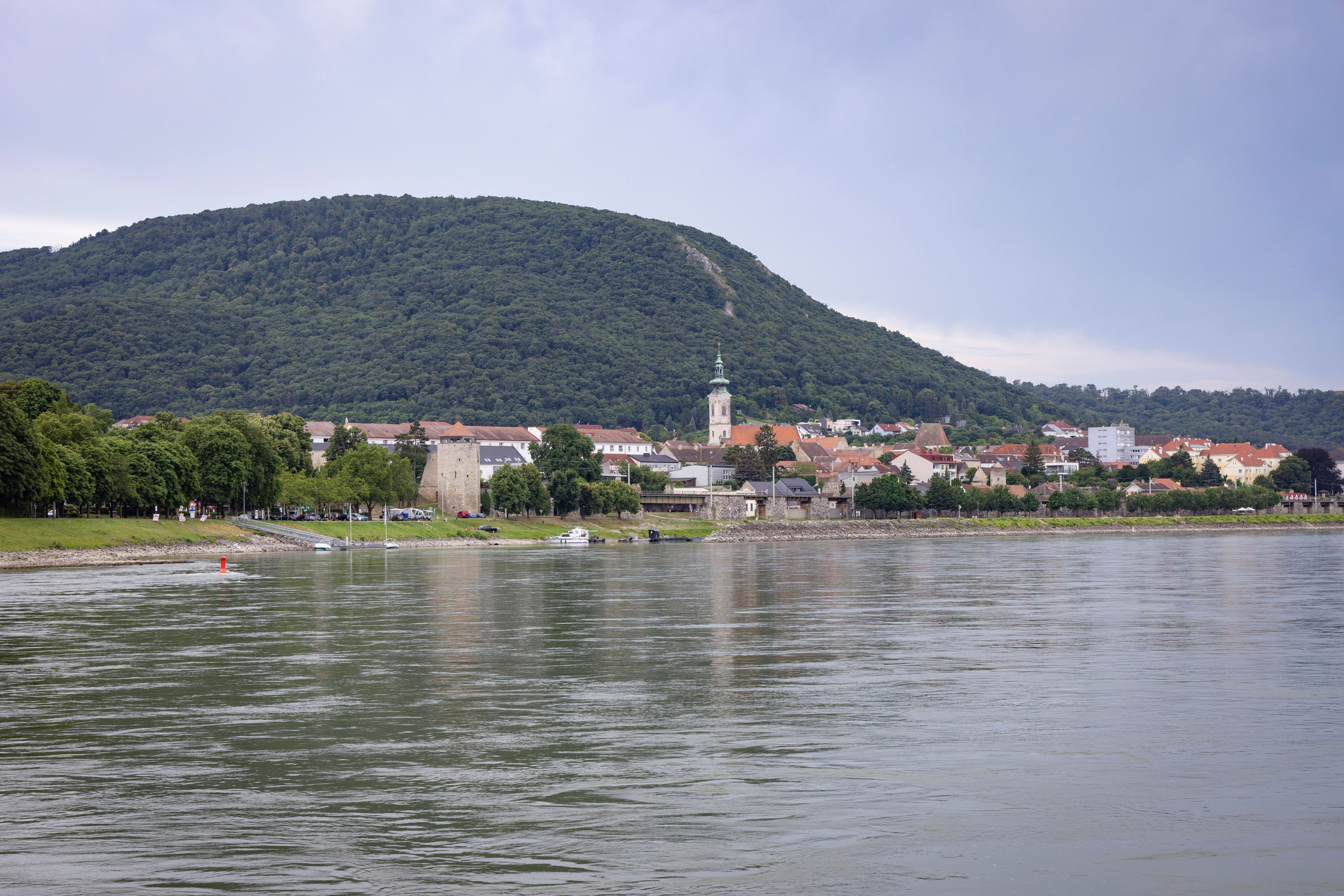 Blick auf Hainburg/Donau am Flussufer mit Hügel im Hintergrund.