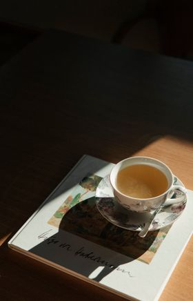 Tasse Kaffee steht auf einem Buch auf einem Tisch im warmen Licht.