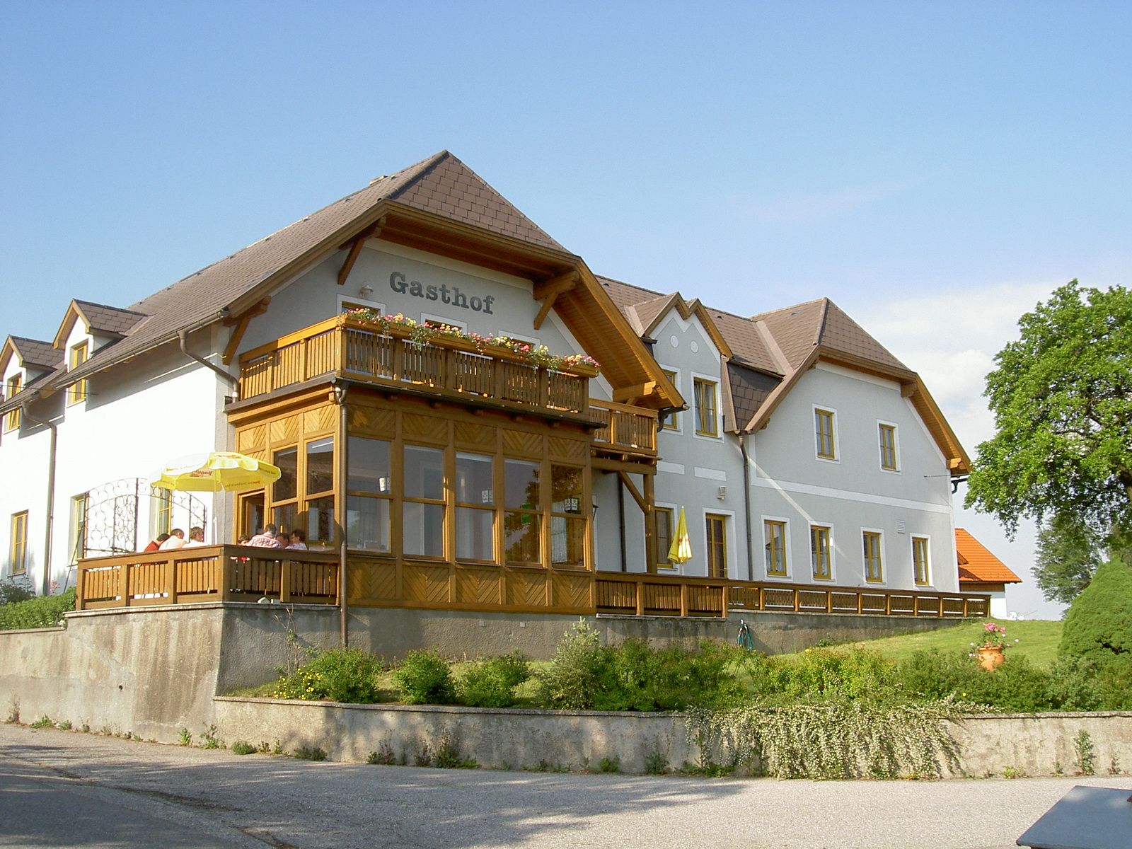 Ein traditioneller Gasthof mit Holzveranda und Blumen auf dem Balkon, umgeben von grüner Landschaft.