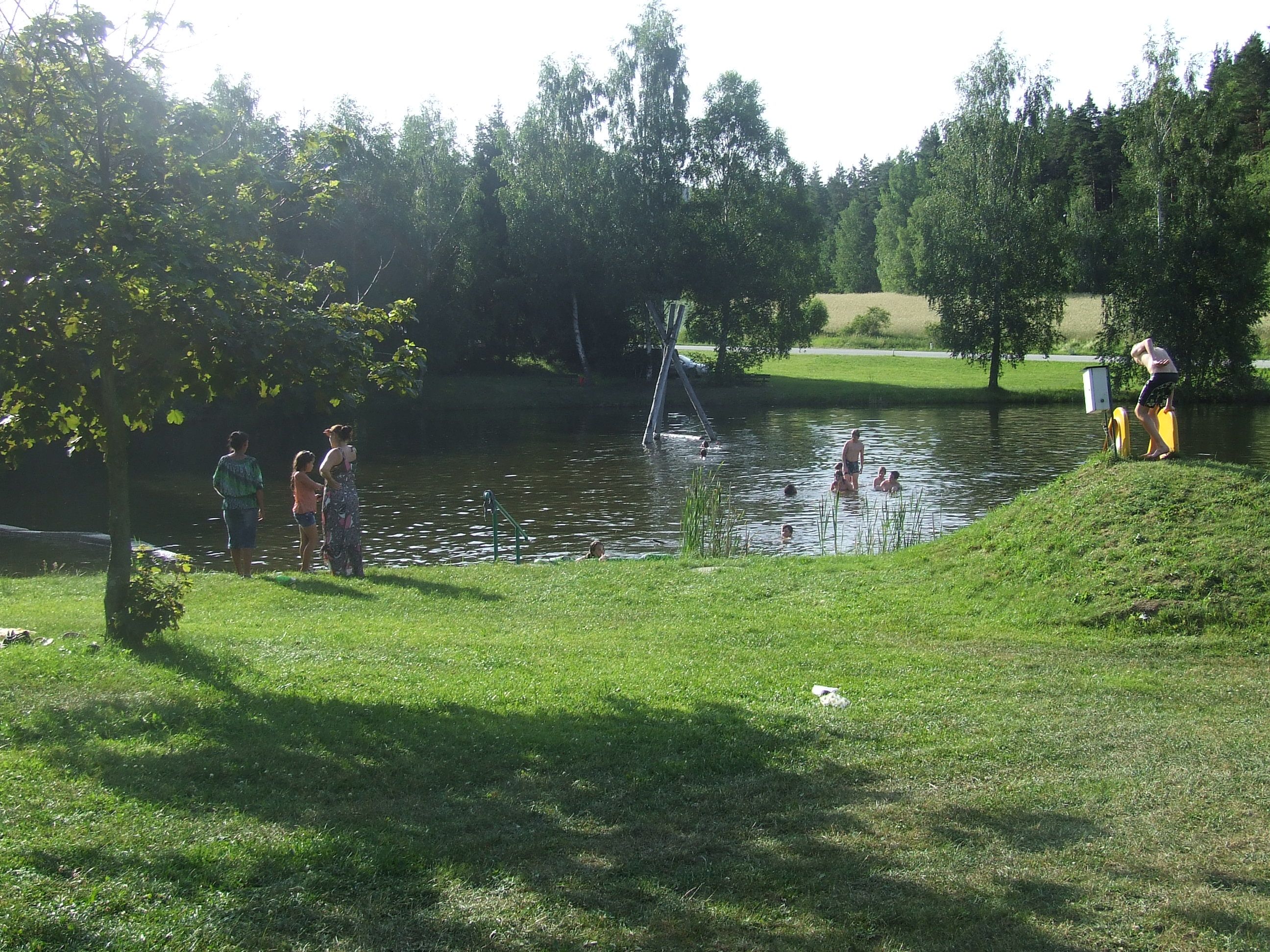 Menschen baden in einem Naturteich umgeben von Bäumen und Wiese.