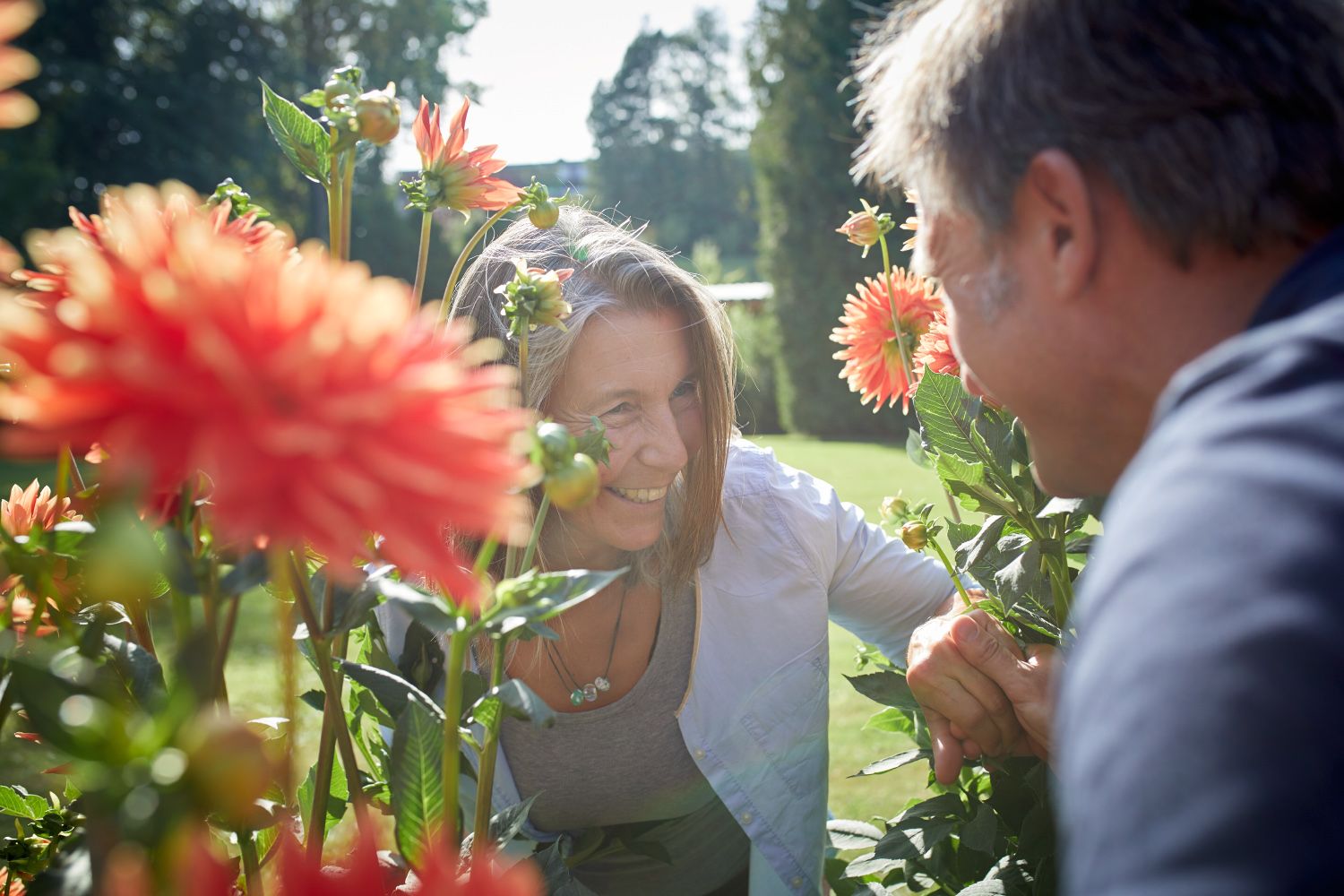 Zwei Personen lächeln sich zwischen blühenden Dahlien im Freien an.