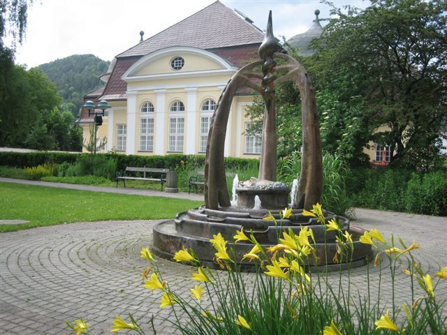 Brunnen vor einem historischen Gebäude mit gelben Blumen im Vordergrund.