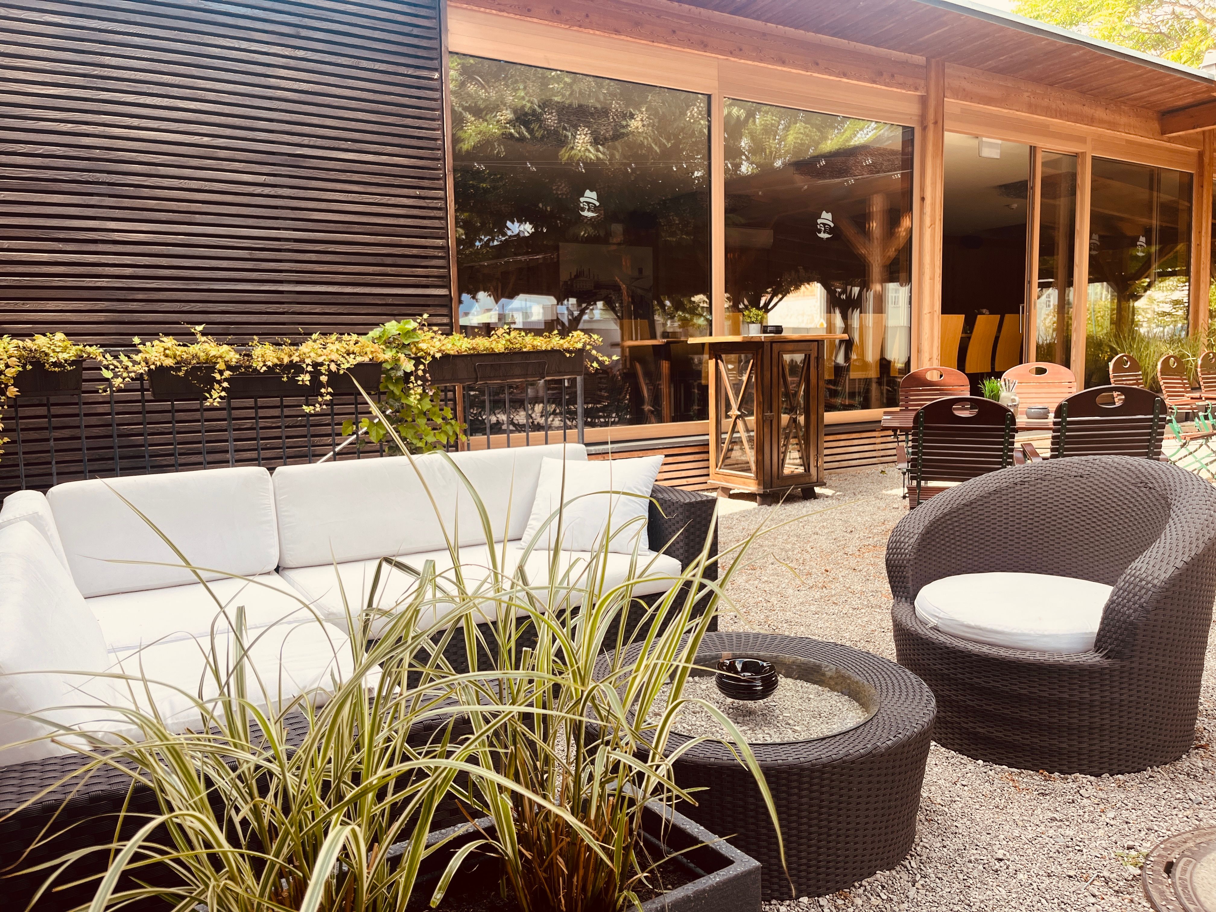 Gemütliche Lounge im Freien mit weißen Sofas, runden Tischen und Pflanzen.