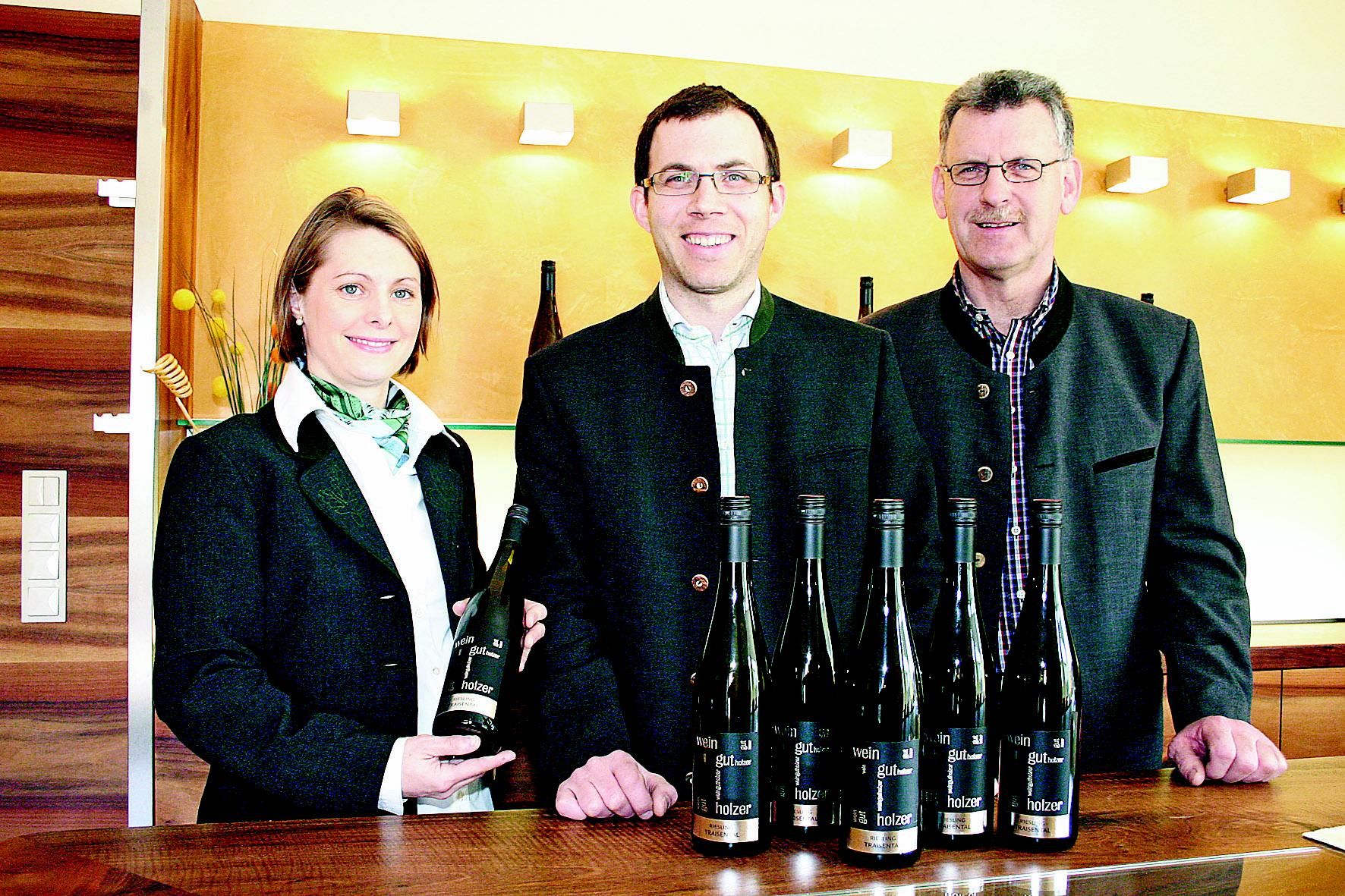 Drei Personen stehen hinter einem Tisch mit Weinflaschen im Weingut Holzer.