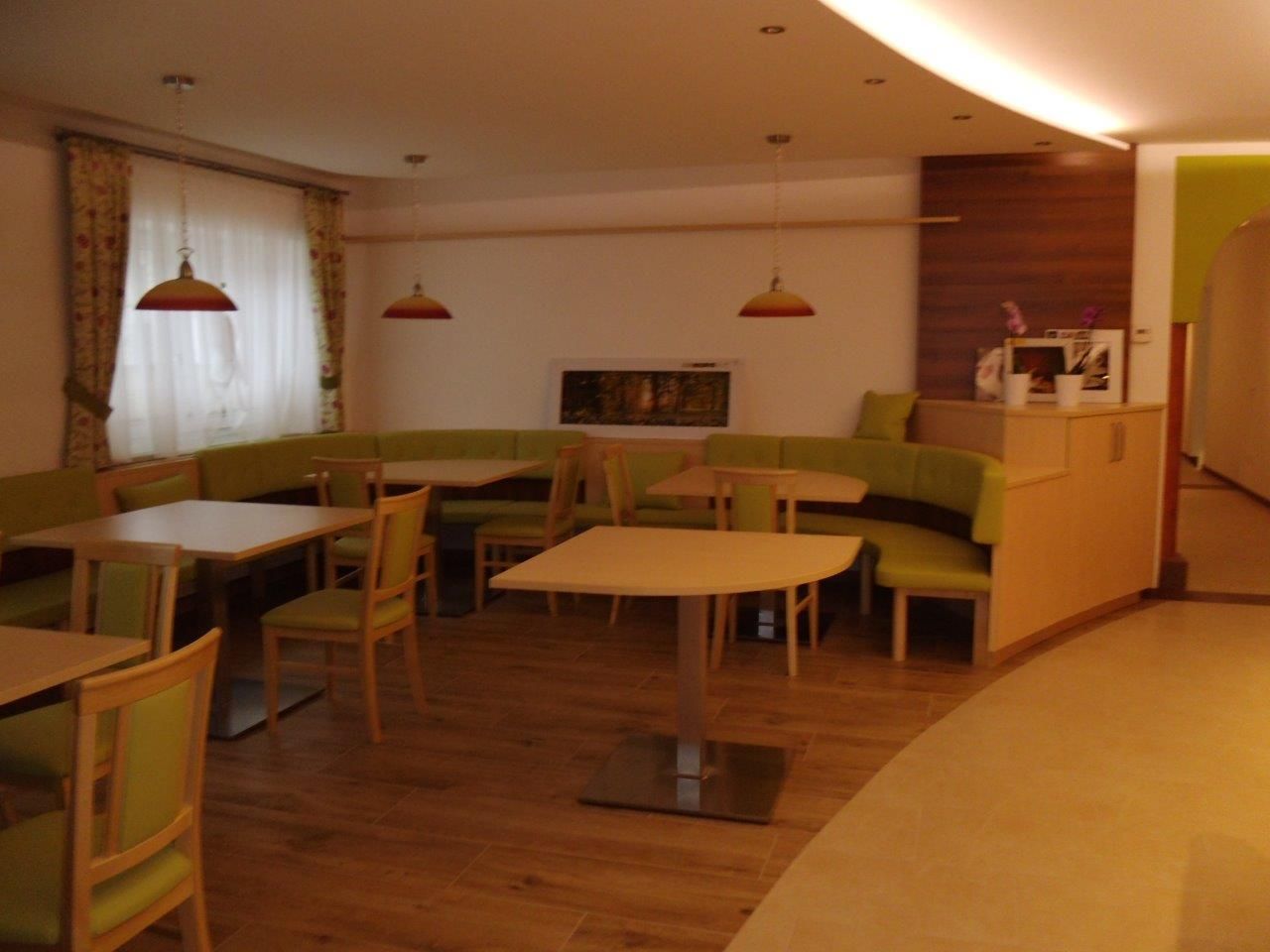 Innenansicht eines Cafés mit grünen Sitzbänken und Holztischen.