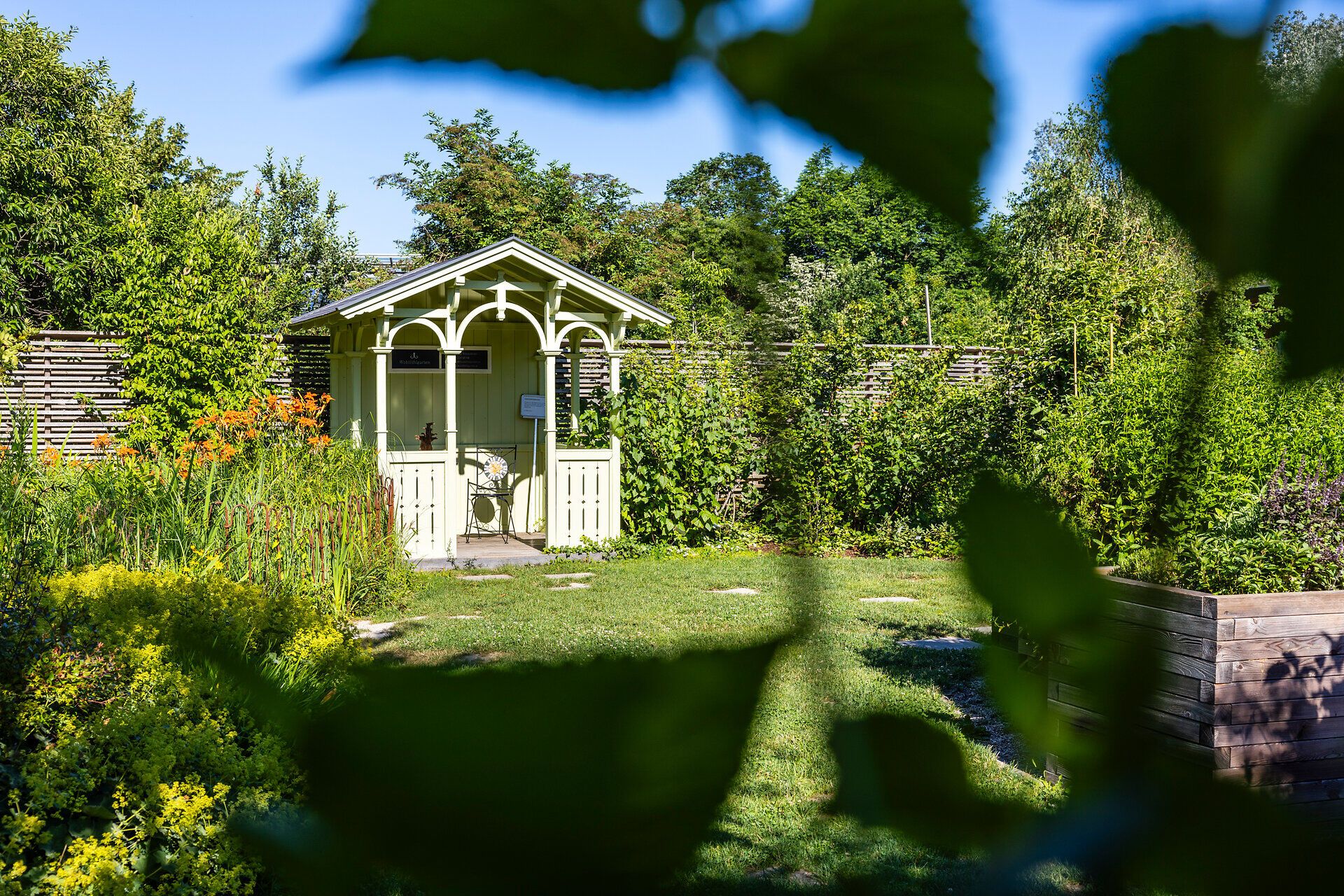 Top Ausflugsziel GARTEN TULLN. Hellgrüner Pavillon aus Holz, grüner Rasen, Büsche und Bäume im Hintergrund, strahlend blauer Himmel und Sonnenschein.