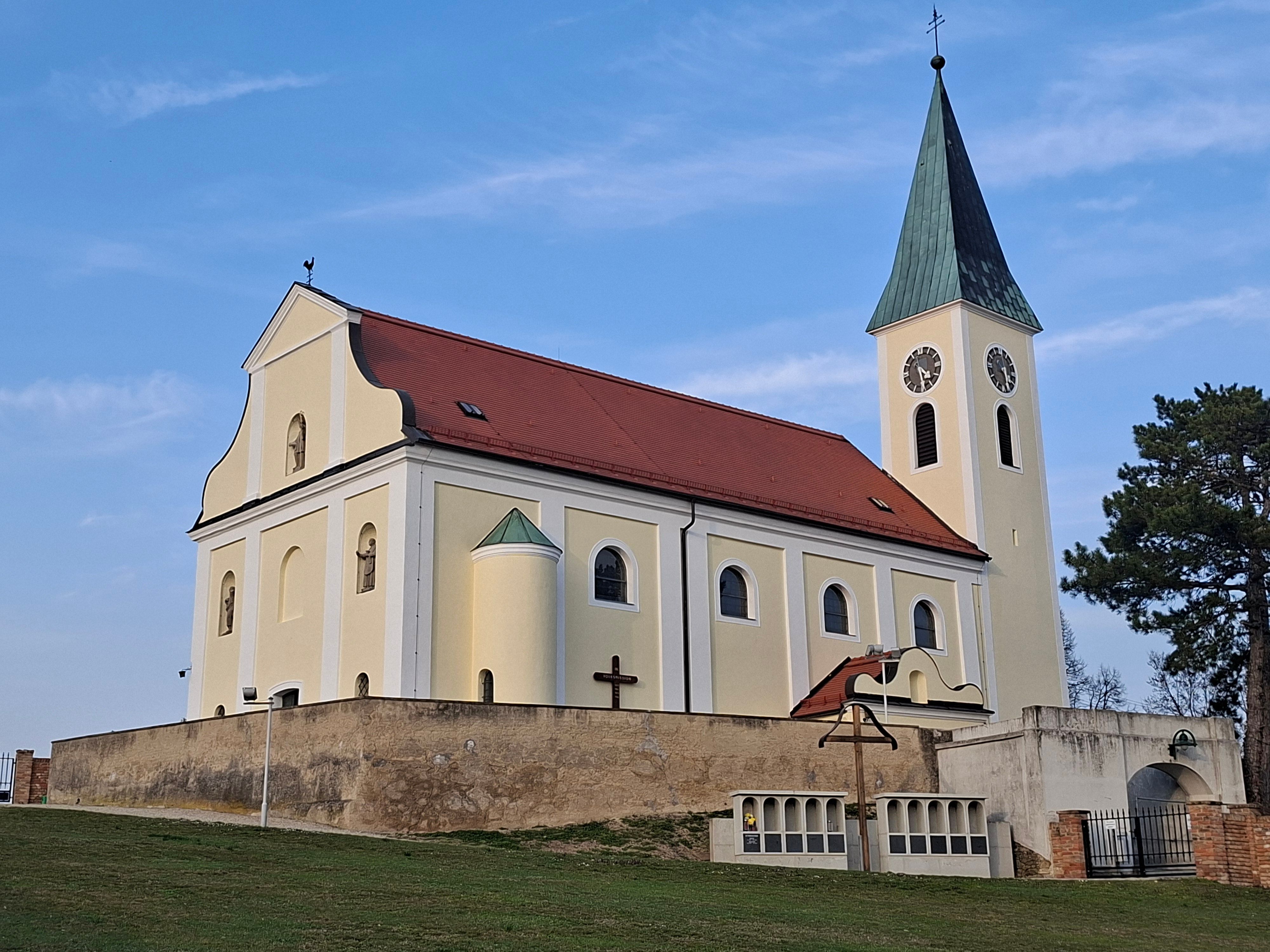 Kirche mit gelber Fassade und rotem Dach vor blauem Himmel.