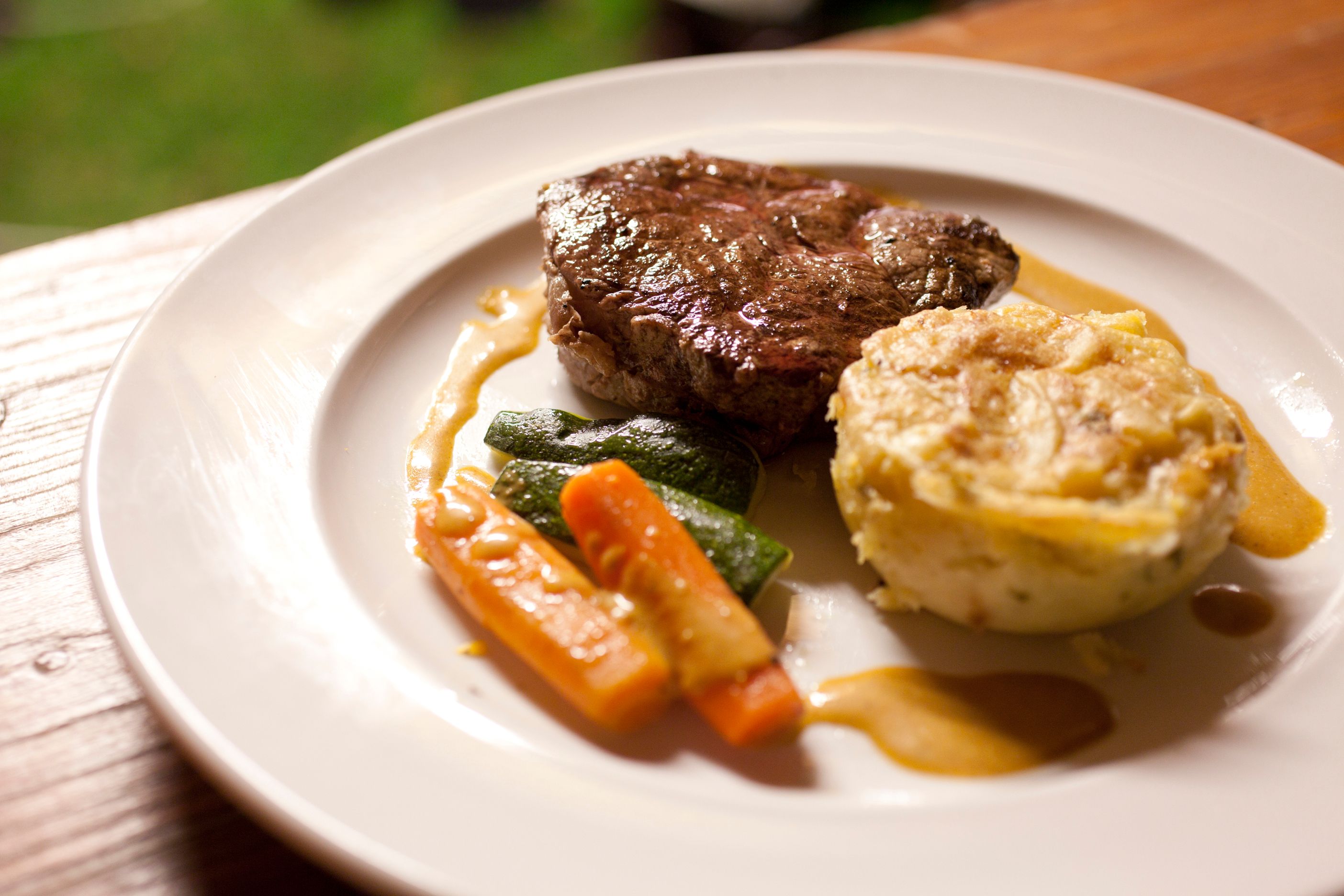 Ein Teller mit einem Stück Fleisch, Gemüse und einem Kartoffelgratin.