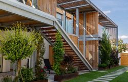 Modernes Gebäude mit weißer Fassade und Holzelementen, umgeben von einer Mauer mit Holztor.