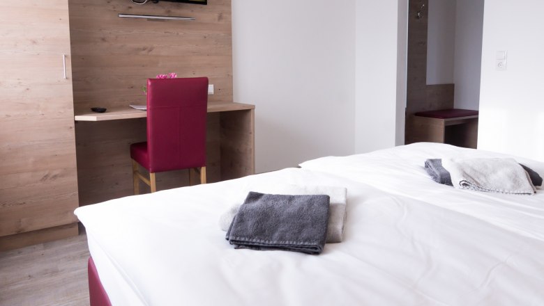 Doppelzimmer mit Bett, Schreibtisch, Stuhl und Fernseher an der Wand.