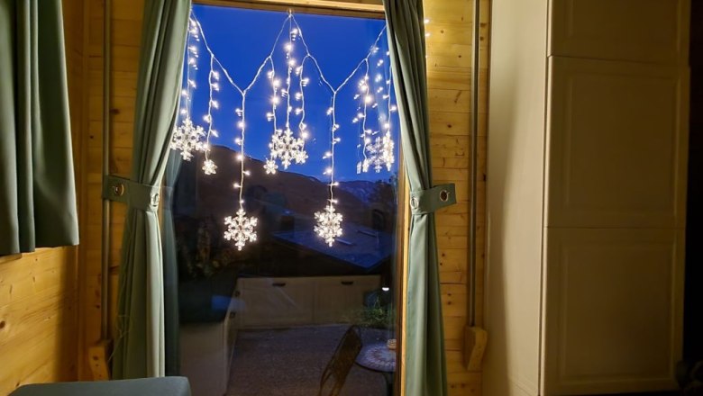 Fenster mit Vorh&auml;ngen und Schneeflocken-Lichterkette, zwei Kerzen auf der Fensterbank.