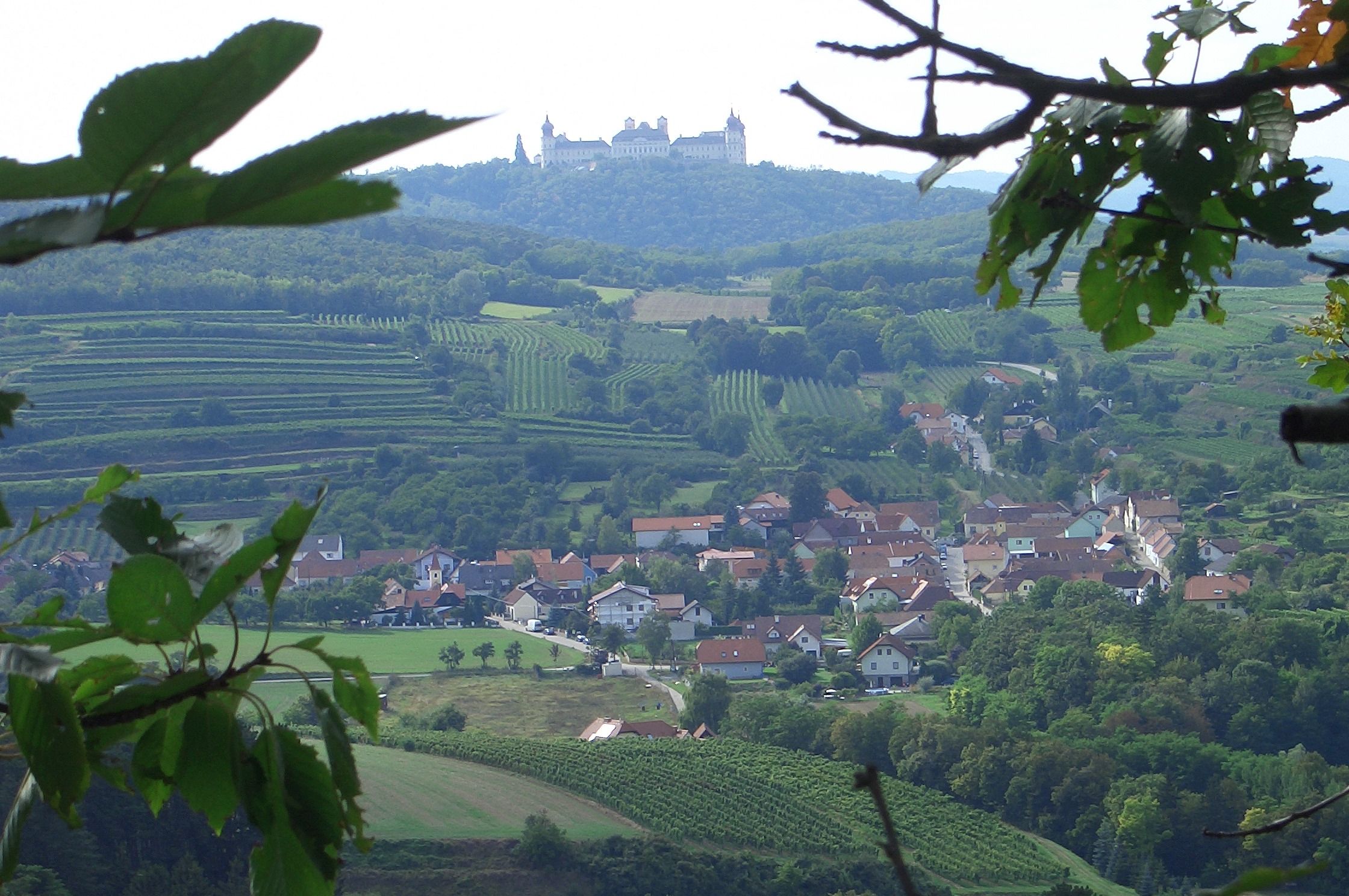 Blick auf Stift Göttweig auf einem Hügel, umgeben von Weinbergen und einem Dorf im Vordergrund.