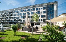 Modernes Gebäude mit vielen Fenstern und Gartenbereich mit Sitzgelegenheiten.