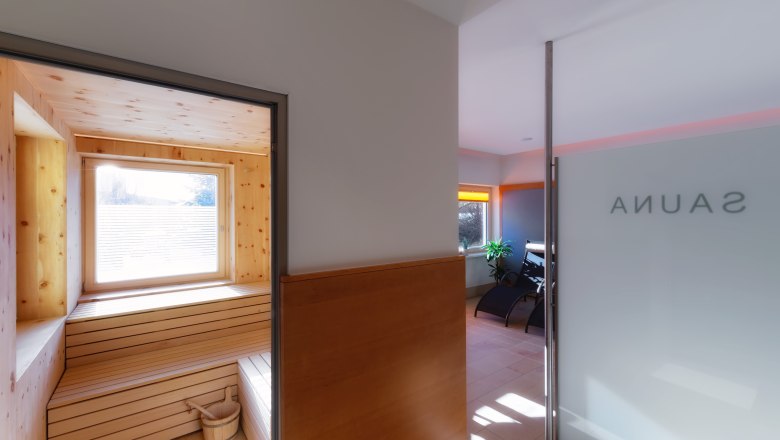 Innenansicht einer Sauna mit Holzverkleidung und Fenster, daneben ein Ruheraum mit Liegestühlen.