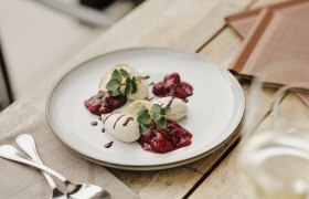 Ein Teller mit Mohnmousse, garniert mit Beerenkompott und Minzbl&auml;ttern, auf einem Holztisch.
