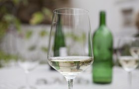 Ein Weinglas mit Wei&szlig;wein im Vordergrund, unscharfe gr&uuml;ne Flasche im Hintergrund.