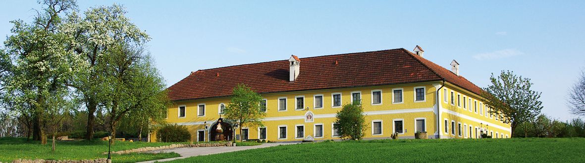 Großes gelbes Gebäude mit rotem Dach in ländlicher Umgebung.