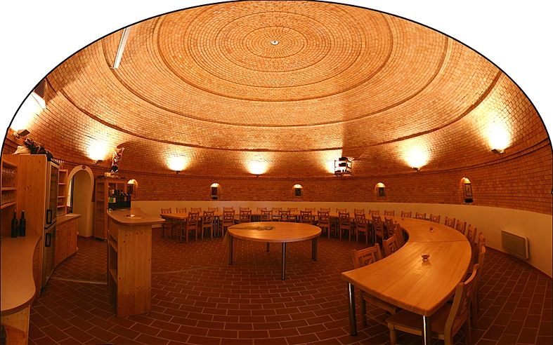 Innenansicht eines runden Weinkellers mit Ziegelwänden und Holzmöbeln.