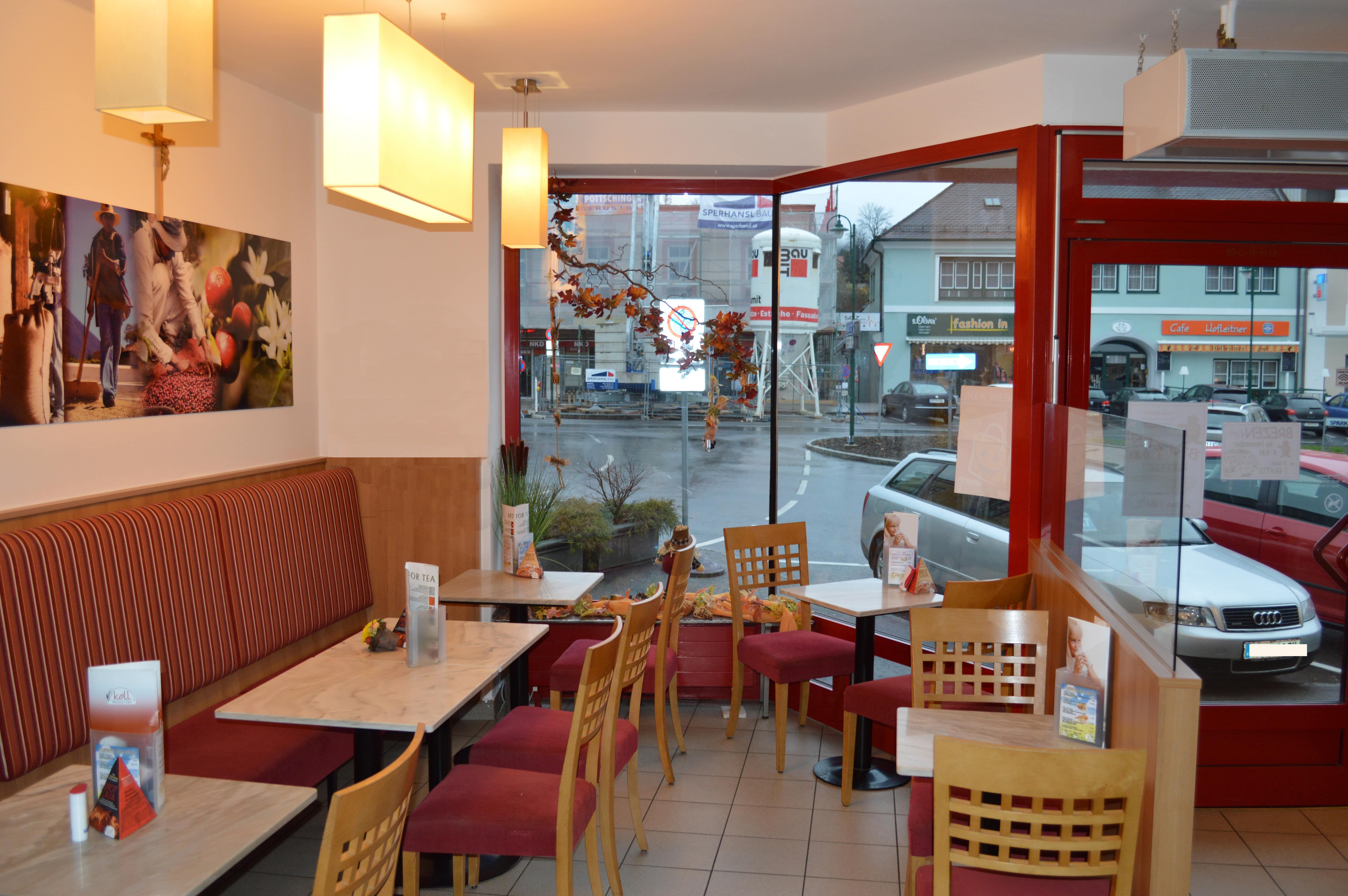 Innenansicht eines gemütlichen Cafés mit roten Stühlen und Tischen, Blick auf eine Straße durch große Fenster.