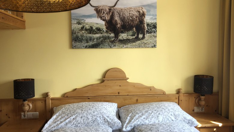Gemütliches Schlafzimmer mit Holzmöbeln, Doppelbett und Bild eines Hochlandrinds an der Wand.
