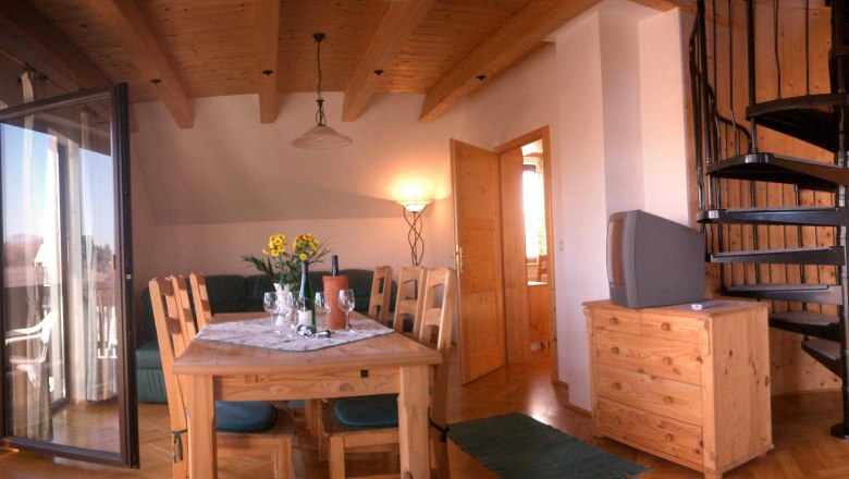 Wohnzimmer mit Holzm&ouml;beln, Esstisch, Wendeltreppe und Balkon.