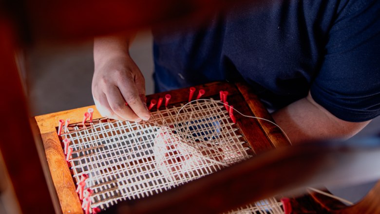 Eine Person repariert ein Thonet Stuhl mit Wiener Geflecht.