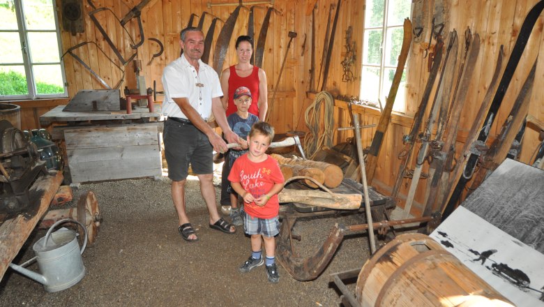 Familie in traditioneller Holzh&uuml;tte mit alten landwirtschaftlichen Ger&auml;ten.